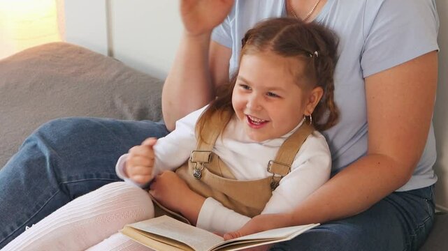 Mother and happy preschool daughter read a book on the bed in a soft and peaceful atmosphere. Focus on early learning and family connection