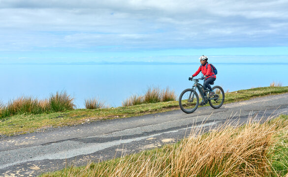 cheerful senior woman riding her electric mountain bike at a rocky beach of the scottiish Atlantic coast near Gairloch, Scotland, UK - Powered by Adobe