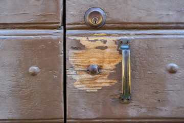 Close-up of an old, weathered wooden door, showing chipped paint, a metal handle, and a deadbolt lock