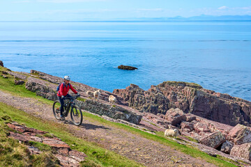 active senior woman riding her electric mountain bike on the cliffs near Rua Reidh Lighthouse next...