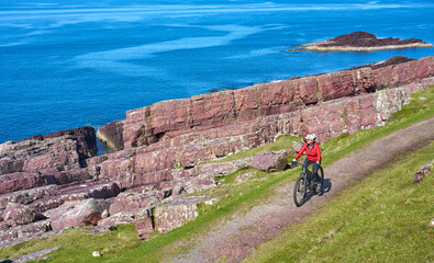 active senior woman riding her electric mountain bike on the cliffs near Rua Reidh Lighthouse next...