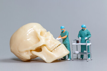 Tiny toy doctors in scrubs perform a delicate and precise surgery on a large human skull model,...