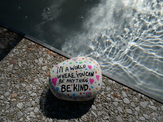 Be kind rock on stone edge by water with surface ripples in sunlight