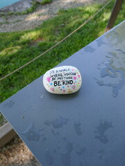 Be kind kindness rock on wet outdoor metal table vertical photo