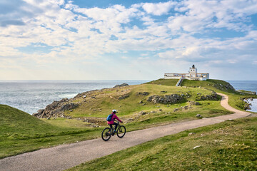 active senior woman riding her electric mountain bike at Strathy  point lighthouse in Northern...