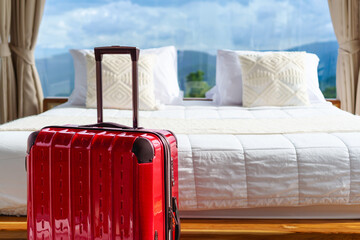 Red suitcase placed in front of a cozy prepared fresh bed with mountain view and cloud sky in natural sun light. Ready for a peaceful vacation in nature. Rainy season.