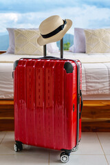 Red suitcase with straw hat placed in front of a cozy prepared fresh bed with mountain view and cloud sky in natural sun light. Ready for a peaceful vacation in nature. Rainy season.
