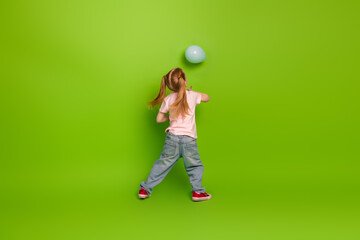 Little girl playing with a blue balloon against a vibrant green background in a casual outfit...