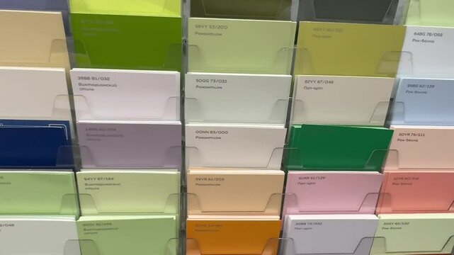 Multicolored paint sample cards displayed on stand in hardware store. Samples are labeled and numbered, custom color mixing available.