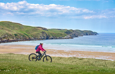 active senior woman riding her electric mountain bike on the cliffs of Strathy  point lighthouse in...