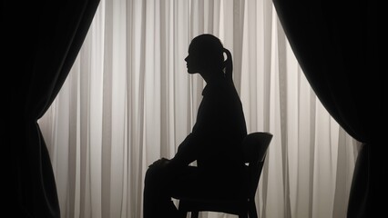 Silhouette of a distressed woman in front of backlit curtains