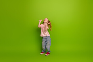 Cheerful young girl with vibrant red sneakers posing in front of a solid green background...