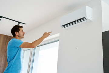 Man using remote control to adjust temperature on wall-mounted air conditioner in modern home...