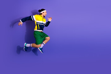 Athletic young man in colorful activewear jumping energetically against a purple background,...
