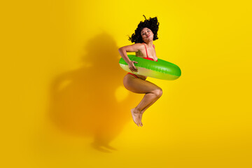 Energetic young woman jumping with an inflatable tube in vibrant summer swimwear against a bright...