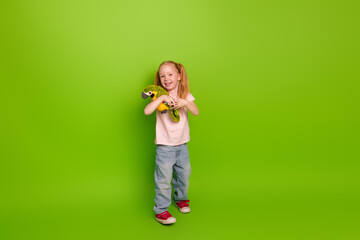 Adorable young girl holding plush snake on bright green background, wearing casual clothing with a...