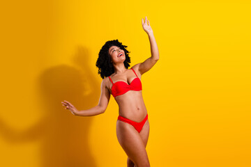 Charming young woman in vibrant red bikini posing joyfully against a bright yellow background...