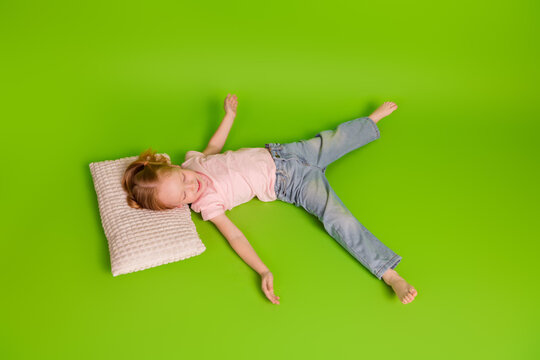 Young girl relaxing on a pillow on bright green backdrop, wearing casual outfit and enjoying leisure time