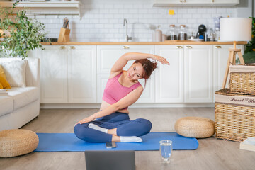 Young athletic woman doing a home workout on an exercise mat, practicing yoga and stretching...