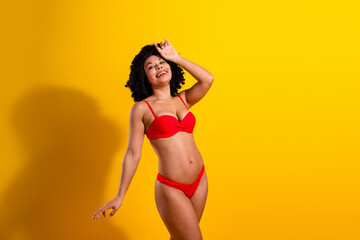 Stylish woman in red bikini posing on yellow background, embracing summer vibes and confidence with...