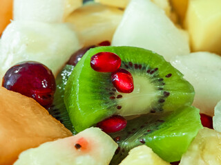 A fruit bowl with kiwi, grapes, melon, pineapple, and pomegranates