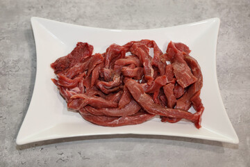 Uncooked beef stir-fry meat strips on a white plate.