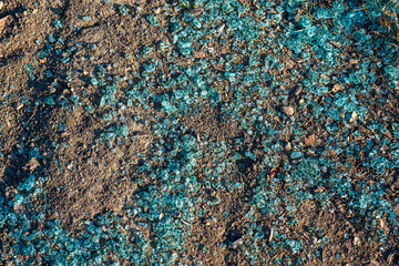 Broken car window glass on the ground. Blue-green safety glass shards scattered on dry soil. Sign...