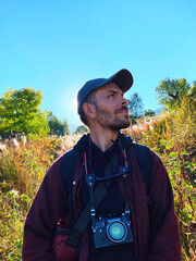 Close-up of a bearded man tourist in profile with a camera with backlight in the back against the blue sky and vegetation in the sunlight. Nature of North Ossetia, protected area