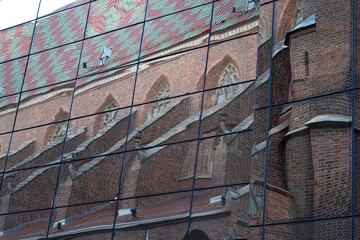 A distorted reflection of the Gothic Church of St. Mary Magdalene in Wroclaw, Poland, captured on the glass facade of a modern building.