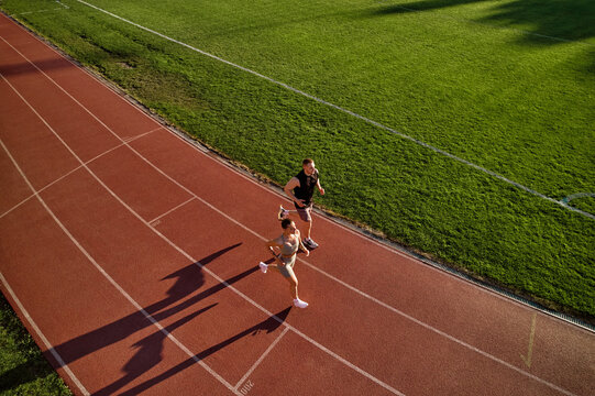 Two people jogging on track beside green field, aerial view