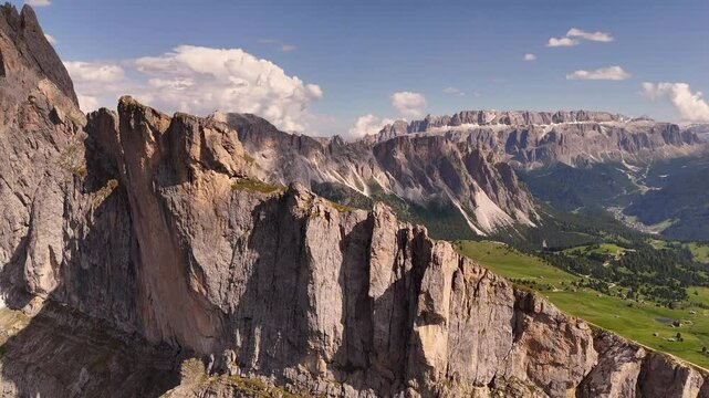 Aerial drone view of Seceda ridgeline in the Italian Dolomites. Iconic jagged peaks emerge from alpine meadows and dramatic cliffs, basking in golden light above Val Gardena in summer
