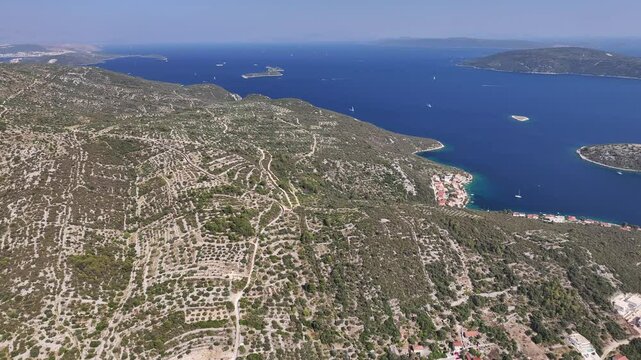 Wide drone panorama showing hills, sea, houses and terrain around Vinisce with layered geography and coastal textures under strong summer sunlight