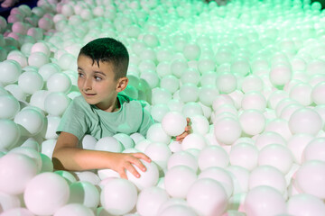 Playful moment in an indoor kids park where a child explores a white ball pit under green lights, highlighting adventure, fun and a sense of curiosity and discovery.