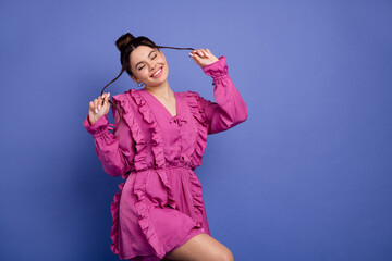 Stylish young woman in pink ruffled dress posing against violet backdrop exuding glamour and trendy...