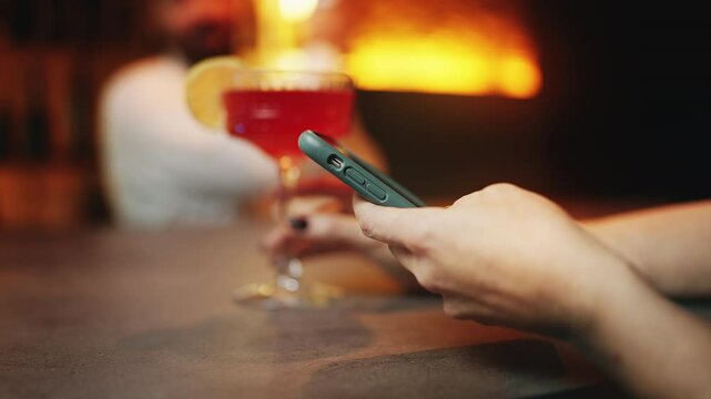 Woman scrolling dating app while drinking cocktail at bar, feeling lonely, bored