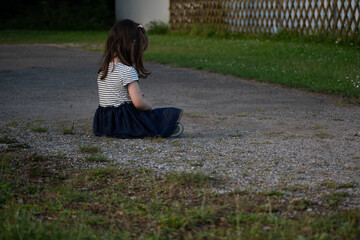 4 yo girl sitting outdoors with her back to the camera, head down, appearing sad or punished. The...
