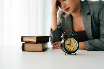 stressed female employee has problems in the morning, feels tired, anxious, confused, and has a clock on her desk in the office.