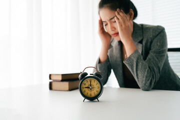 stressed female employee has problems in the morning, feels tired, anxious, confused, and has a clock on her desk in the office.