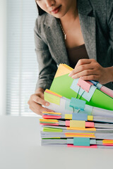 Young female employee is working with a pile of documents to search for information and check documents on the table. Document search concept.