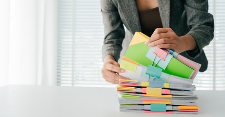 Young female employee is working with a pile of documents to search for information and check documents on the table. Document search concept.