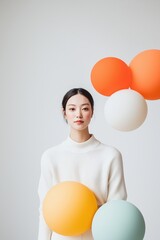 Young woman holding colorful balloons in studio. Smiling with casual attire