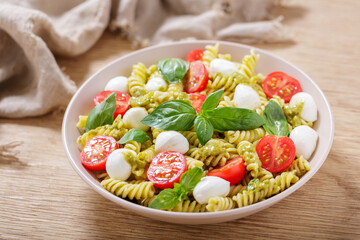 plate of pesto pasta salad, tomatoes, green basil and mozzarella