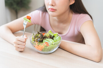 Diet in bored face, unhappy beautiful asian young woman, girl on dieting, holding fork at tomato on salad plate, dislike or tired with eat fresh vegetables. Nutrition of clean, healthy food good taste