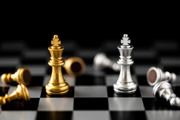 Gold and silver king chess pieces stand among fallen pawns on a chessboard. Business strategy...