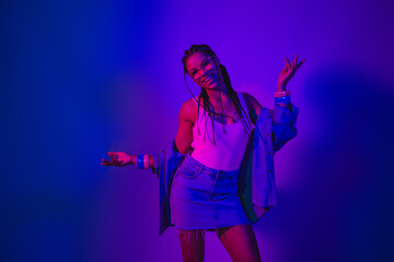 Stylish young woman in neon lighting shows positive gestures wearing modern casual denim fashion for nightlife
