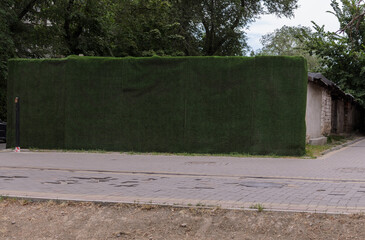 the wall of the old building is covered with a green fabric of synthetic turf