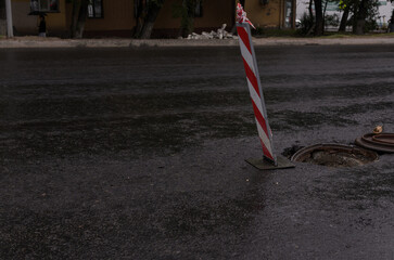 red and white road fence post in front of an open road hatch on a rainy evening