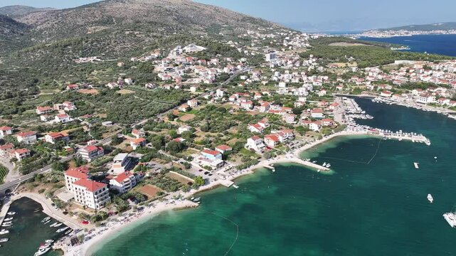 Drone captures stunning natural and built environment of Seget Vranjica with houses, trees and coastal textures in warm daylight from an elevated viewpoint
