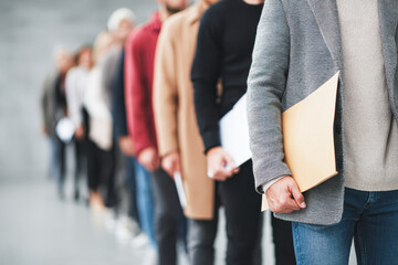 Fototapeta premium People standing in a line, dressed in casual and business casual attire, holding documents, possibly waiting for an interview or appointment.