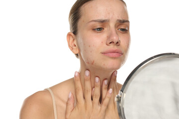 Studio shot of young woman examining her skin in mirror on white background